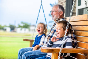 Abuelo sonriente disfrutando en un columpio con sus nietos, símbolo de tranquilidad y felicidad alcanzada gracias a una jubilación bien planificada