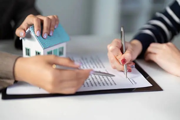 Personas firmando un contrato de compraventa con maqueta de casa sobre la mesa, simbolizando los gastos de compra de vivienda en España