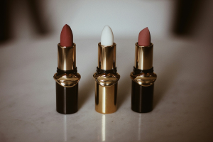 Tres barras de labios abiertas sobre una superficie clara, con envases dorados y detalles en forma de labios, representando productos cosméticos recibidos como muestras gratuitas por internet en España.